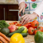 Woman wearing apron slicing a variety of colorful vegetables