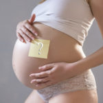 Belly of a young pregnant woman with a white sticker and a quest