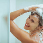 Smiling young woman washing head with shampoo
