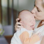 Close up of young mother holding her crying baby daughter, kissing her
