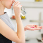 Closeup on young housewife eating pills and drinking water