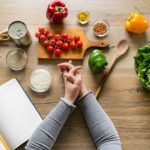 woman-leaning-on-table-with-various-ingredients-and-a-diet-planning-book