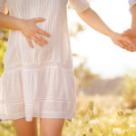 Happy and young pregnant couple hugging in nature