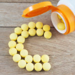 Yellow pills forming shape to C alphabet on wood background