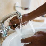 Cropped hands of man filling water in glass at sink
