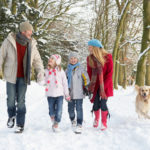 Family Walking Dog Through Snowy Woodland