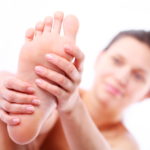 Young woman massages her foot. On a white background.