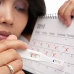 Sad woman with negative pregnancy test and calendar