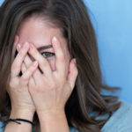 Studio shot of brunette girl hiding eyes under hand while feeling ashamed.