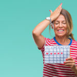 Middle age senior hispanic woman holding menstruation calendar over isolated background stressed with hand on head, shocked with shame and surprise face, angry and frustrated. Fear and upset for mistake.