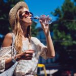 Trendy woman drinking a water from bottle, outdoors.