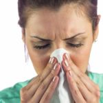 Close-up of woman suffering from cold with tissue on mouth