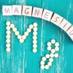 magnesium-spelled-out-with-wooden-blocks-on-turquoise-wooden-background-with-round-magnesium-tablets-spelling-out-mg