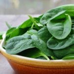 Baby spinach leaves in stoneware bowl on rustic wooden table