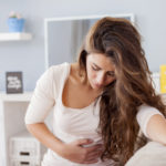 Young woman sitting on the bed with hard stomach pain
