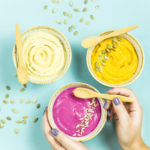 a woman holds a beetroot sauce next to bright snacks – hummus of chickpeas and carrot sauce among pumpkin seeds. Top view. Flat lay