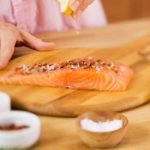 Woman Squeezing a Lemon Wedge over Salmon