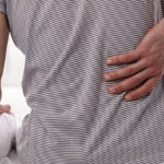 Man suffering from back pain at home in the bedroom. Uncomfortable mattress and pillow causes back pain.