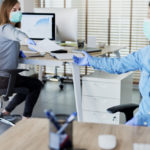 Two people in office passing documents with keeping a distance