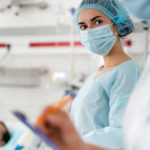 Nurse in sterile cap and protective mask standing in hospital room
