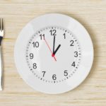 Dinner plate with clock face on wooden table with fork an knife