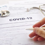 COVID-19 Health insurance concept. Blurring of hand holding pen and Stethoscope on health form. Focus on ” COVID-19 “