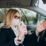 Business woman in protection mask sitting inside a car using antiseptic