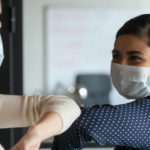 Smiling,Diverse,Female,Colleagues,Wearing,Protective,Face,Masks,Greeting,Bumping