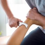 Physiotherapist massaging woman’s leg using tools