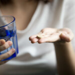 Female hands holding pill and glass of water, closeup view