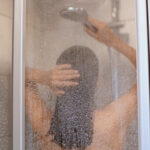 Enjoying a shower. Back view of beautiful young slim shirtless woman taking shower, washing hair in bathroom, hygiene, healthy and beauty, indoor shot.