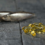 A pile of capsules with fish oil on the background of two fish on a wooden table.