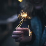 Burning sparklers in the hands of a young woman in the dark.