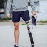 Cut out picture of caucasian handicapped sporty man standing outdoors with sneaker in hand.