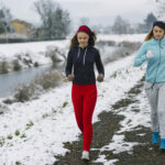 two-female-athlete-jogging-street-near-river-winter