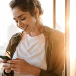 Image of adorable woman holding smartphone at terrace outdoors