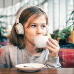 A little girl in headphones in a cafe with a cup of tea.