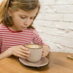 Little girl at table in cafe with big cup of art drink