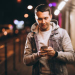 Young handsome man using phone at night in the street