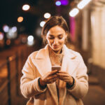 Young woman using phone outside the night street