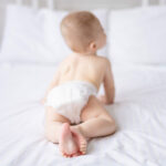 a healthy baby naked in panties crawls on the bed on white bedding, the child turned his back