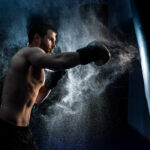 Male boxer boxing in punching bag. shot in smoke. Black background