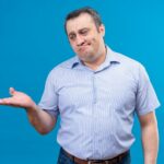 troubled-upset-middle-aged-man-blue-striped-shirt-raising-hand-blue-background_141793-21890