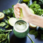 A woman is squeezing a lemon on a green juice of healthy, fresh