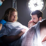 Doctor examining pregnant woman during delivery while man holding her hand in operating room