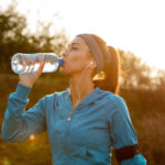 Thirsty runner refreshing herself with water while jogging in the morning.